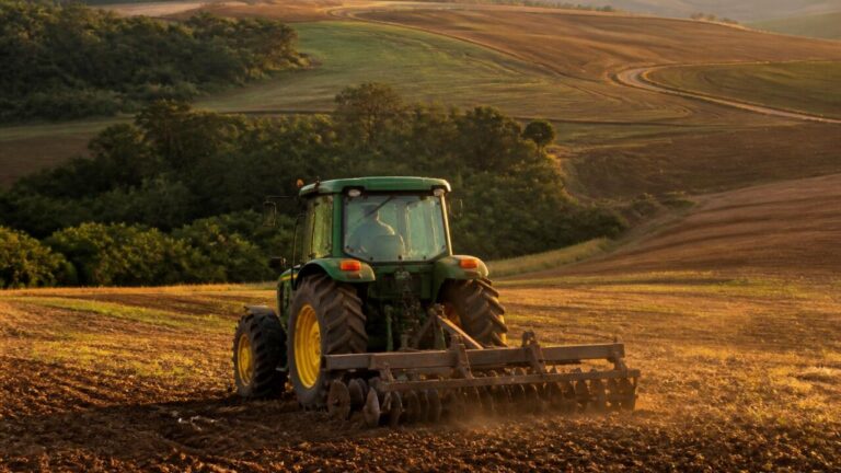 Trator operando em terreno agrícola com colinas e vales ao fundo