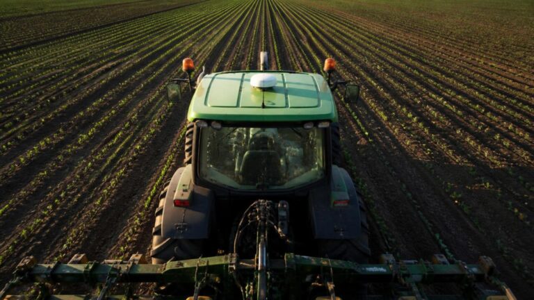Trator com sistema de orientação guiando passadas precisas em campo agrícola visto de cima.