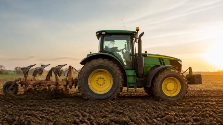 Trator agrícola visto de lado com implemento acoplado em campo arado