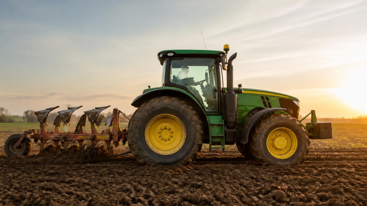 Trator agrícola visto de lado com implemento acoplado em campo arado